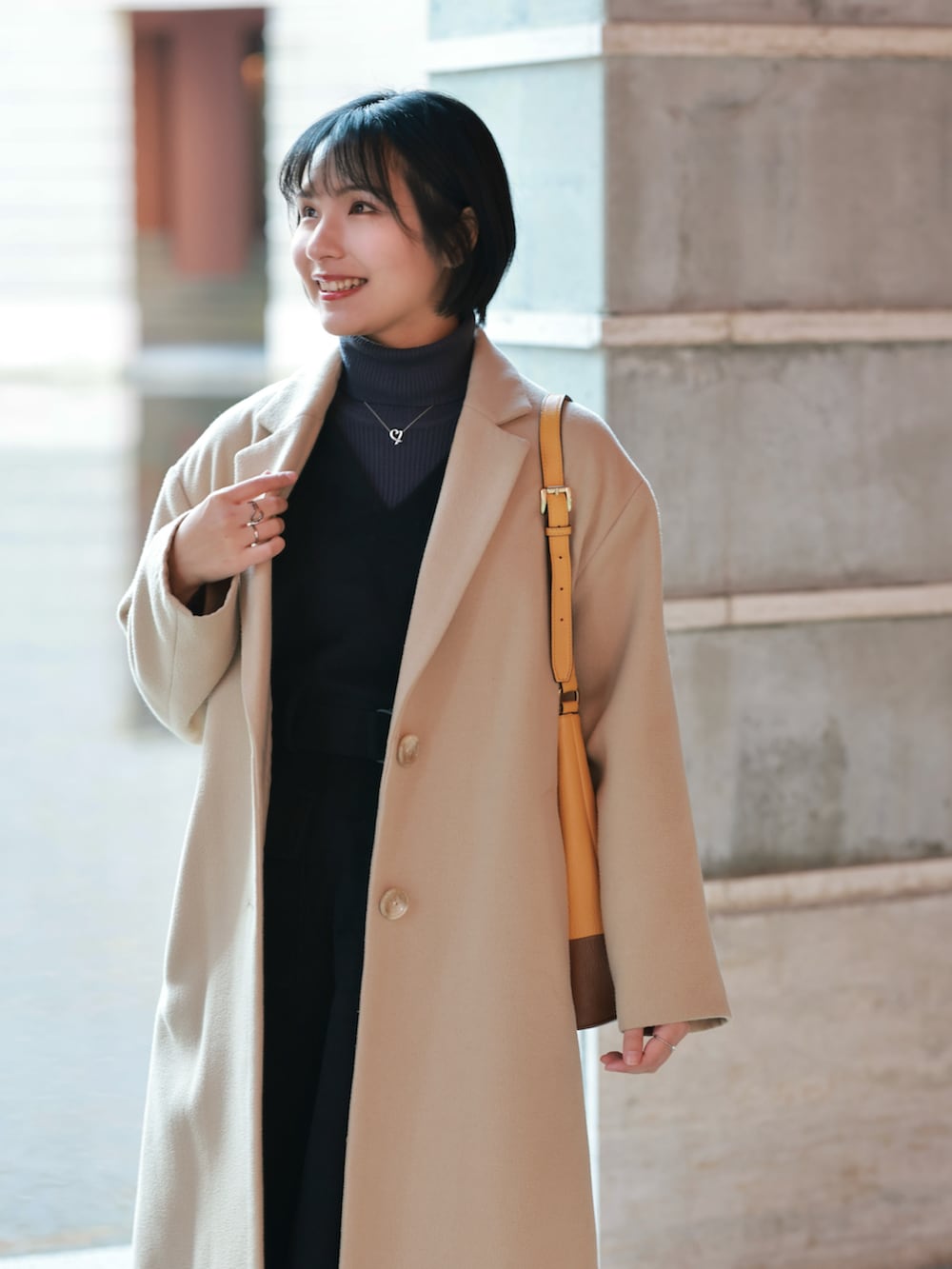 ベージュ系のチェスターコート、ブラック系のジャンパースカート、ブラック系のブーティを着用したレディースの冬コーディネートの5枚目の写真