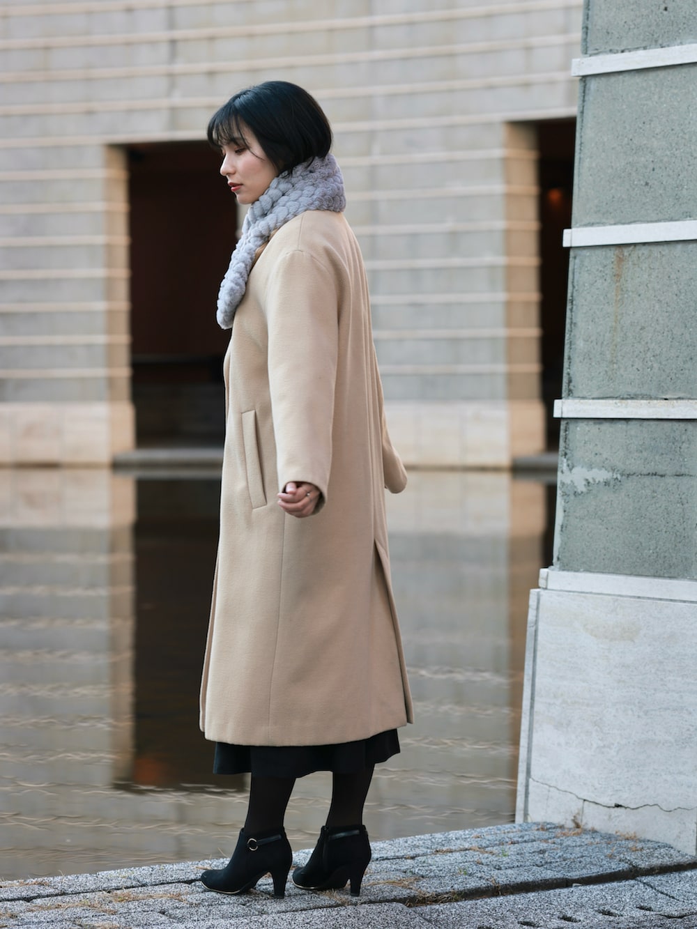 ベージュ系のチェスターコート、ブラック系のジャンパースカート、ブラック系のブーティを着用したレディースの冬コーディネートの4枚目の写真