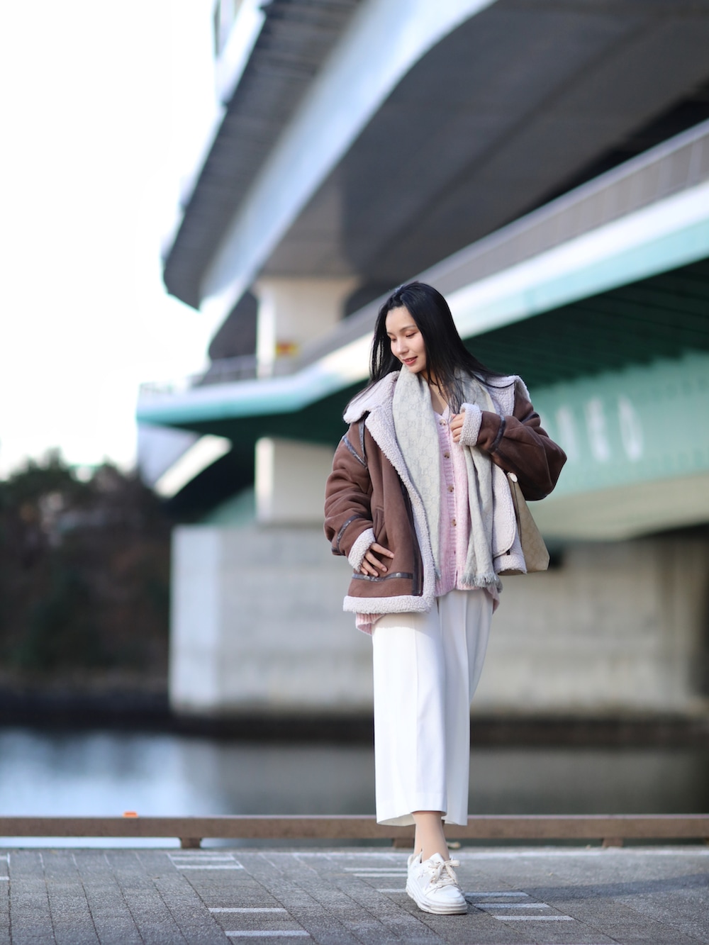 ブラウン系のムートンコート、ピンク系のニット/セーター、ホワイト系のスニーカーを着用したレディースの冬コーディネートの3枚目の写真