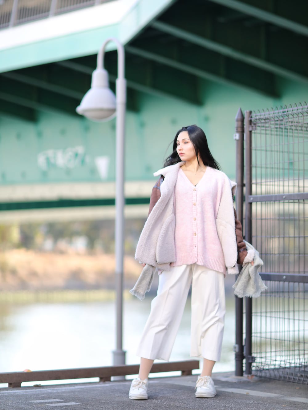 ブラウン系のムートンコート、ピンク系のニット/セーター、ホワイト系のスニーカーを着用したレディースの冬コーディネートの2枚目の写真