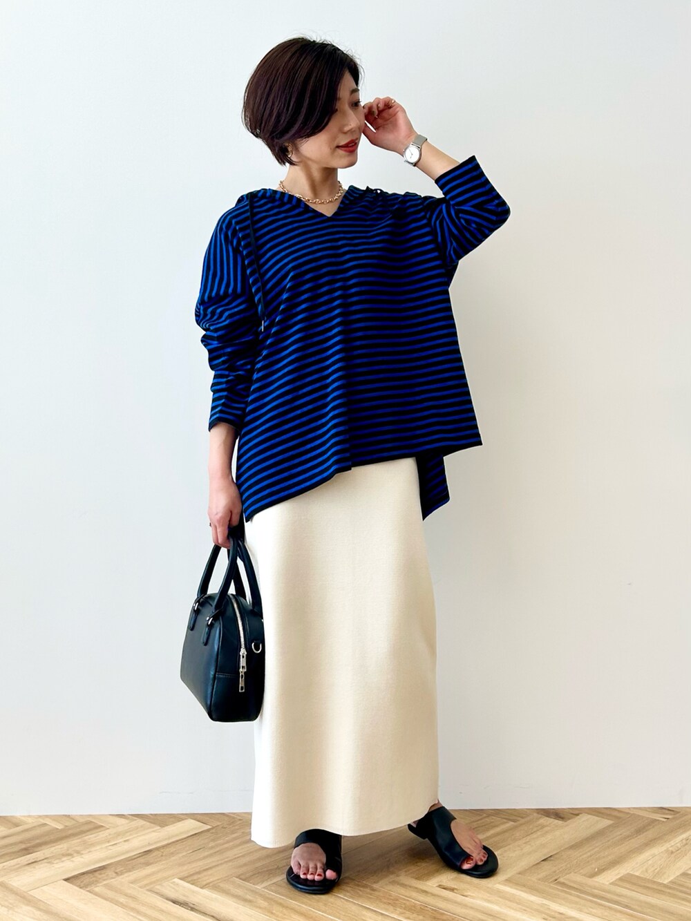 ブルー系のチュニック、ホワイト系のスカート、ブラック系のボストンバッグを着用したレディースの春コーディネートの2枚目の写真