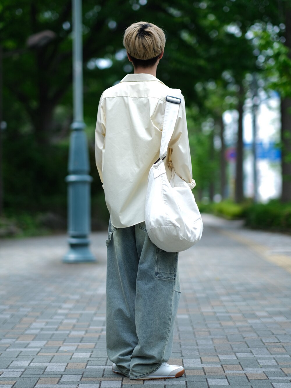 ブルー系のデニムパンツ、ホワイト系のスニーカー、ホワイト系のショルダーバッグを着用したメンズの夏コーディネートの2枚目の写真