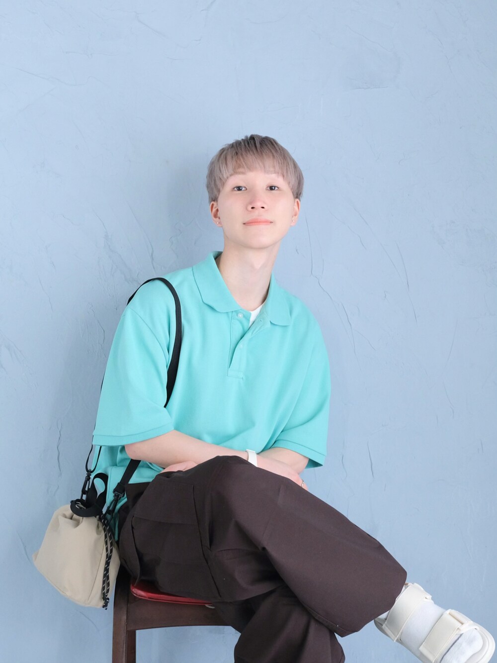 ホワイト系のサンダル、ブルー系のポロシャツ、ベージュ系のショルダーバッグを着用したメンズの春コーディネートの2枚目の写真