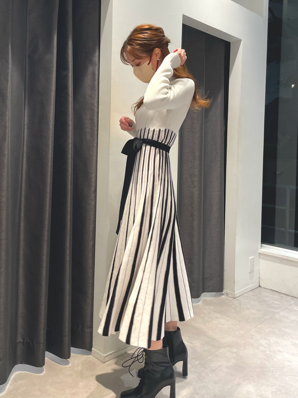 ホワイト系のワンピース、ベージュ系のチェスターコート、ブラック系のブーツを着用したレディースの冬コーディネートの6枚目の写真