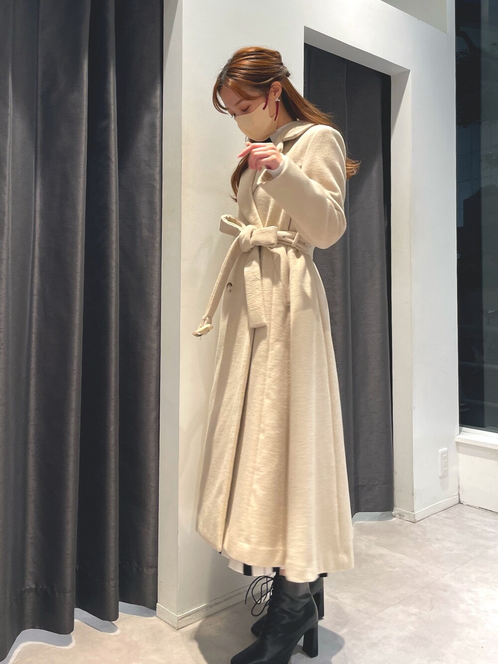 ホワイト系のワンピース、ベージュ系のチェスターコート、ブラック系のブーツを着用したレディースの冬コーディネートの2枚目の写真