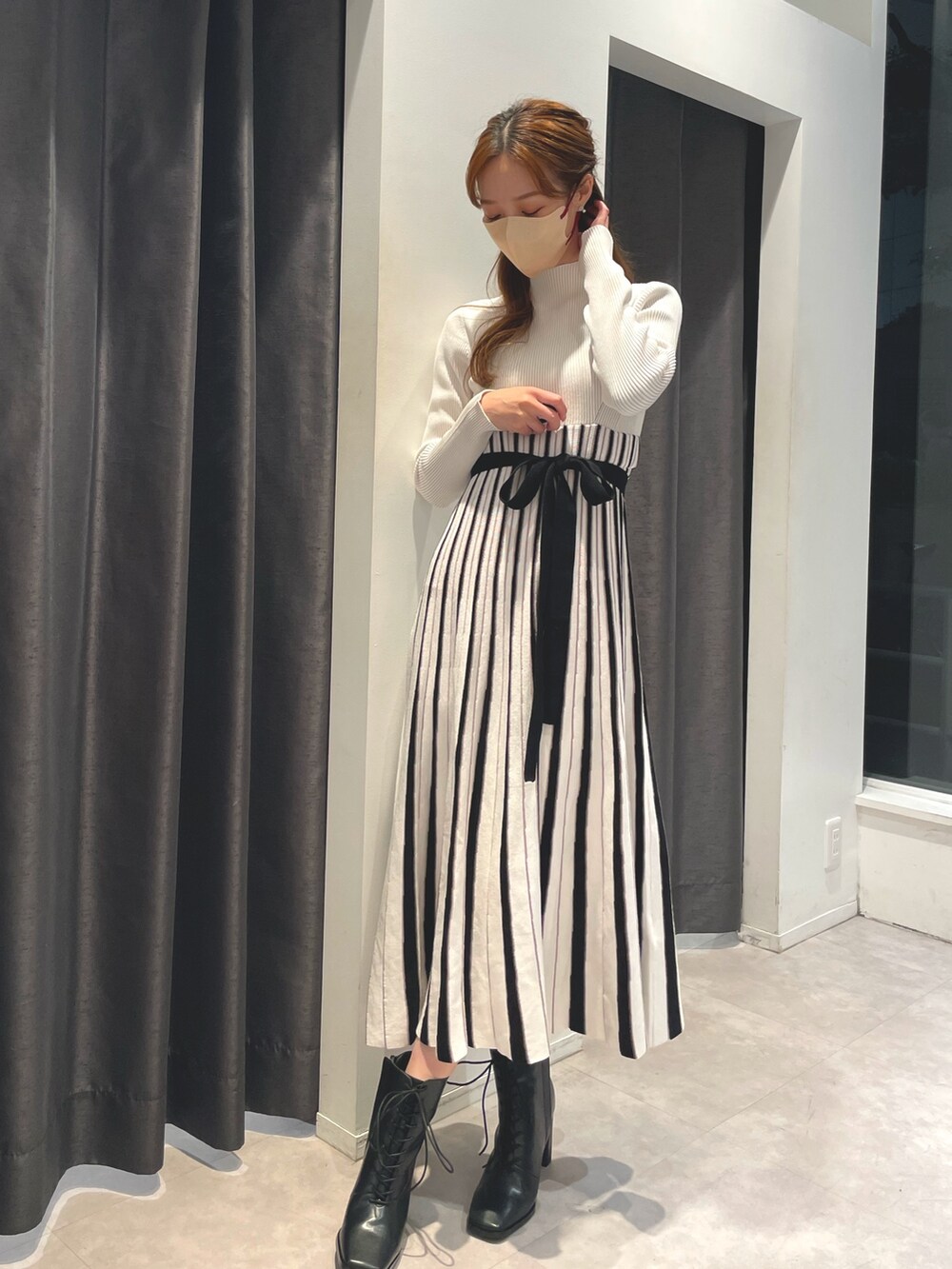 ホワイト系のワンピース、ベージュ系のチェスターコート、ブラック系のブーツを着用したレディースの冬コーディネートの5枚目の写真