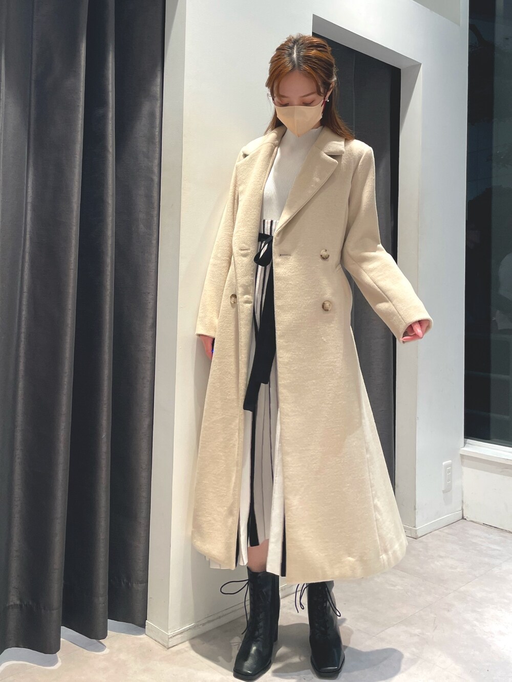ホワイト系のワンピース、ベージュ系のチェスターコート、ブラック系のブーツを着用したレディースの冬コーディネートの4枚目の写真