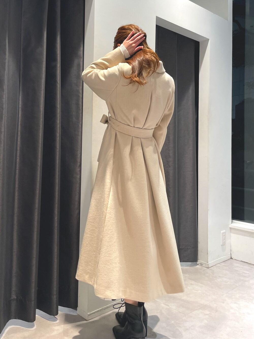 ホワイト系のワンピース、ベージュ系のチェスターコート、ブラック系のブーツを着用したレディースの冬コーディネートの3枚目の写真