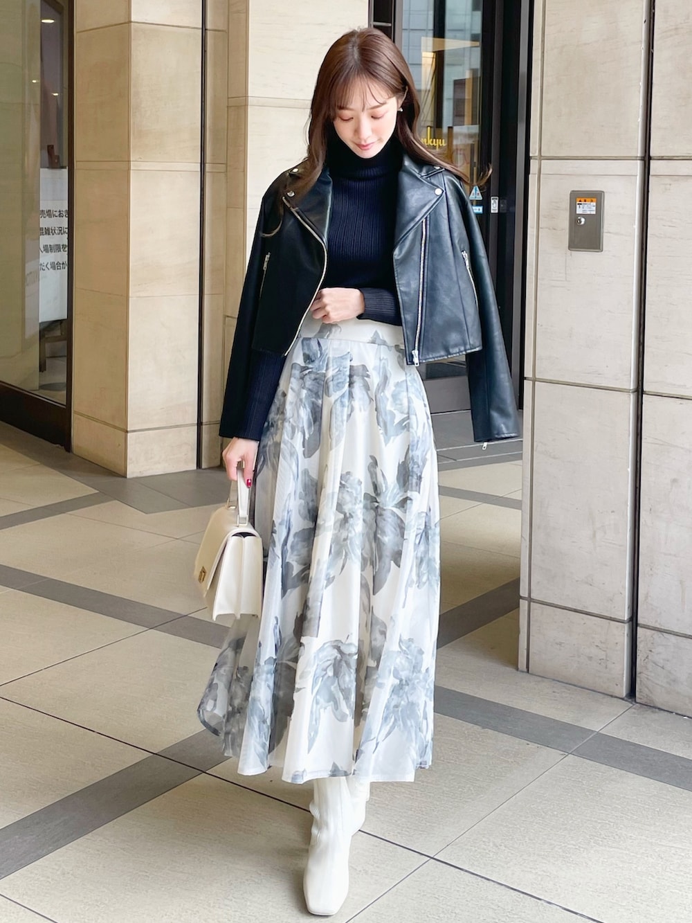 ブラック系のライダースジャケット、ブラック系のニット/セーター、ホワイト系のスカートを着用したレディースの冬コーディネートの2枚目の写真