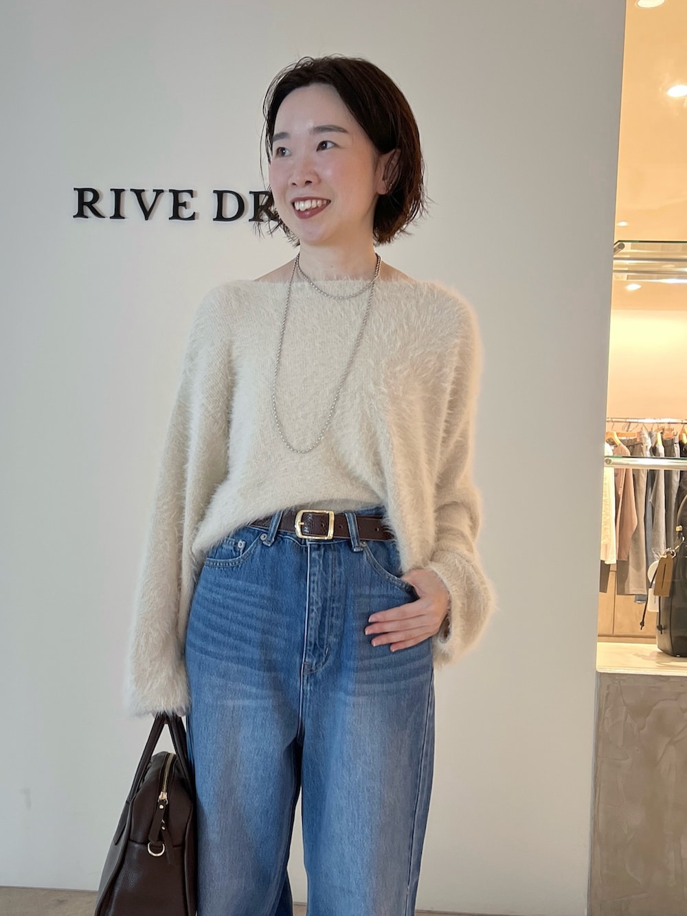 ブルー系のデニムパンツ、ホワイト系のニット/セーター、ブラウン系のボストンバッグを着用したレディースの秋コーディネートの4枚目の写真