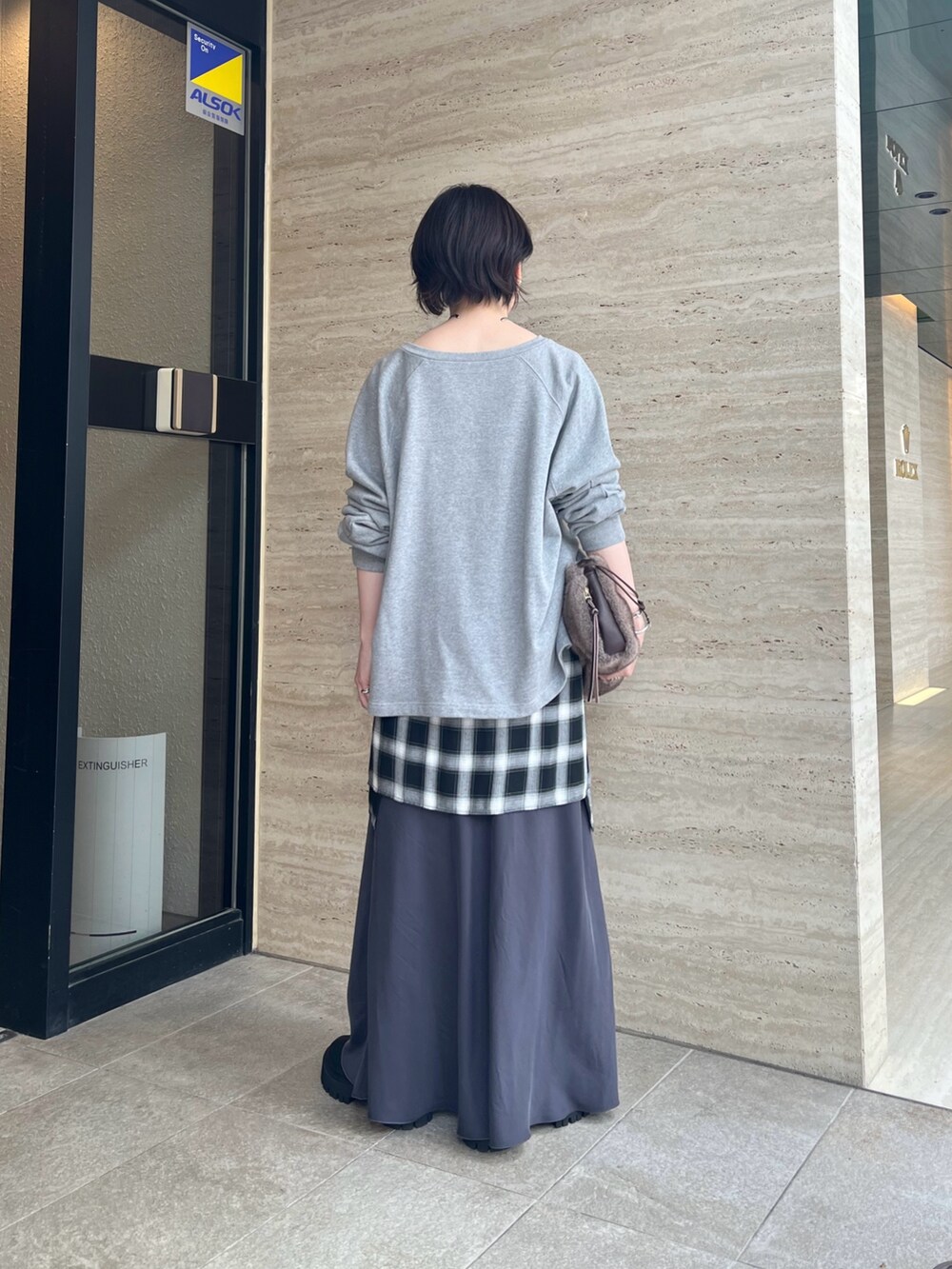 グレー系のスウェット、グレー系のスカート、ブラウン系のハンドバッグを着用したレディースの夏コーディネートの3枚目の写真