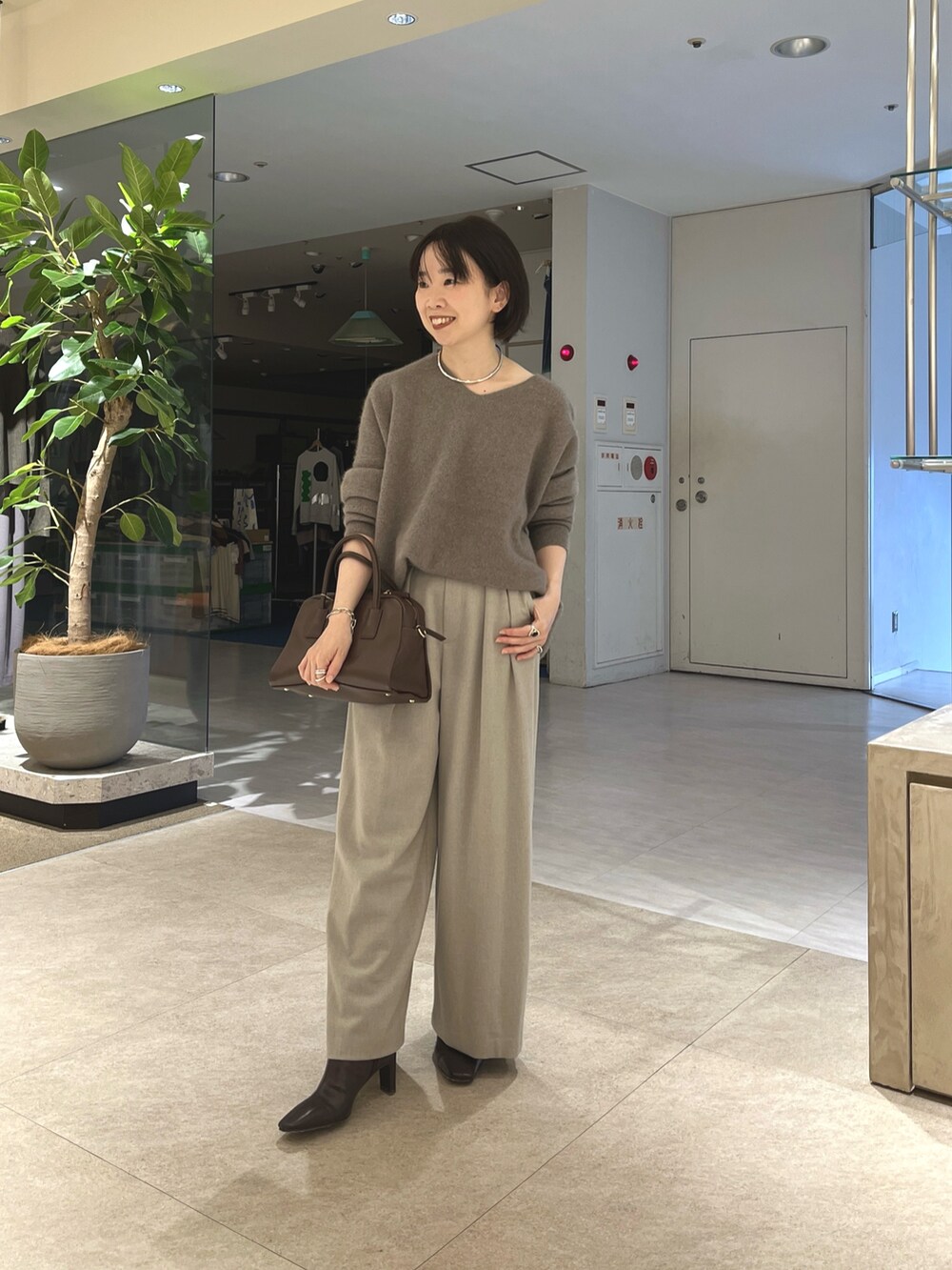 グレー系のニット/セーター、ベージュ系のスラックス、ブラウン系のボストンバッグを着用したレディースの秋コーディネートの4枚目の写真