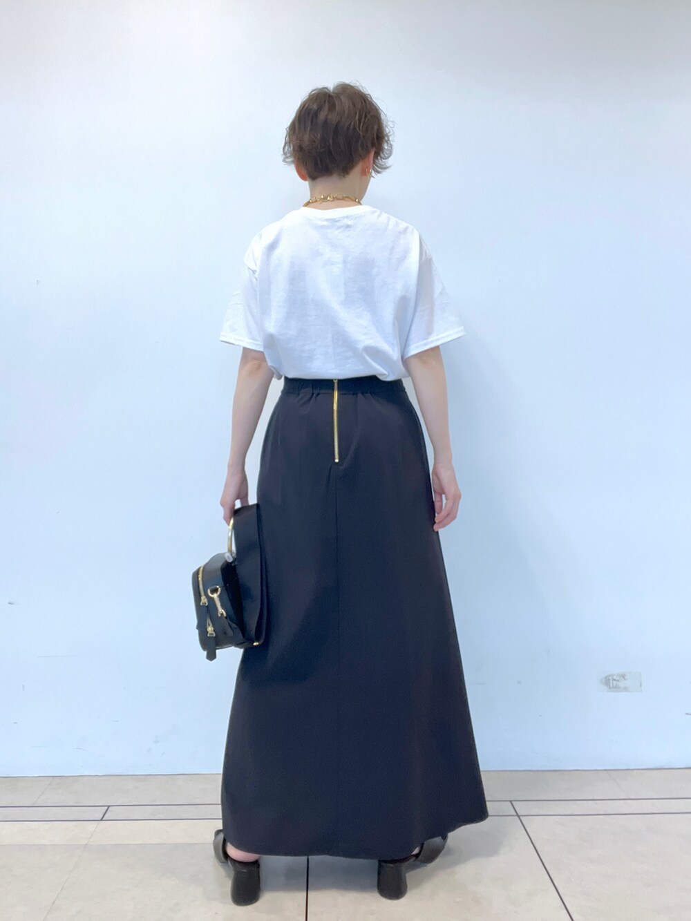 ブラック系のスカート、ホワイト系のTシャツ/カットソー、ブラック系のサンダルを着用したレディースの春コーディネートの3枚目の写真