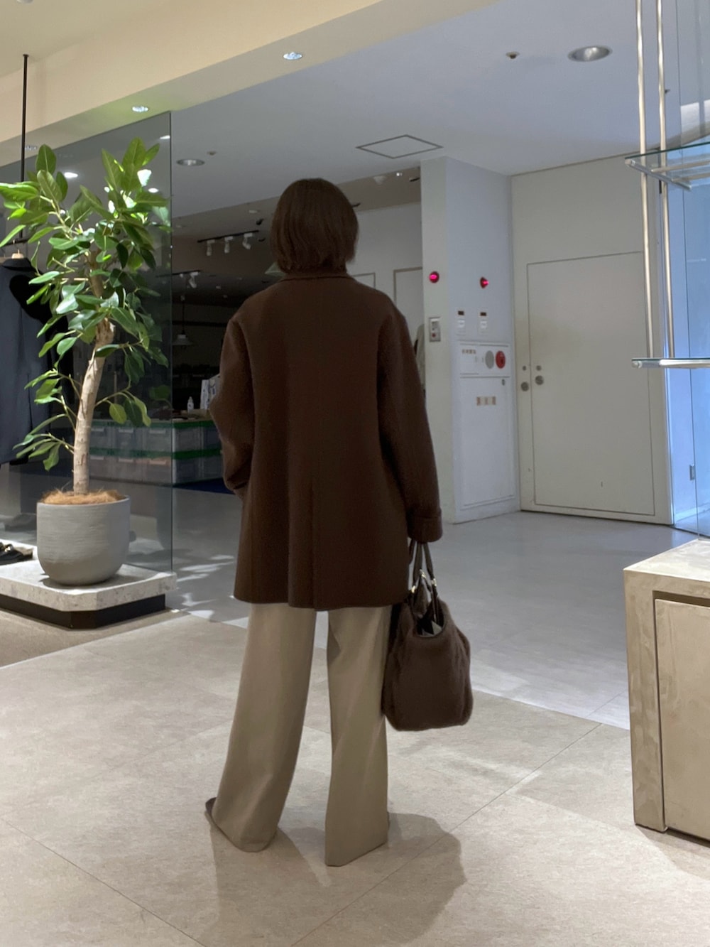 ブラウン系のトートバッグ、ベージュ系のスラックス、ブラウン系のブーツを着用したレディースの秋コーディネートの3枚目の写真