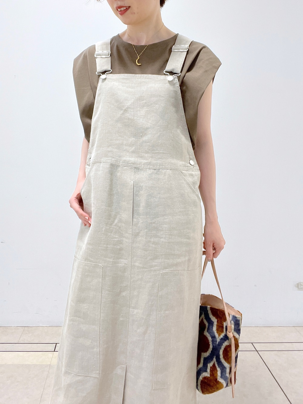 ブラウン系のトートバッグ、ベージュ系のジャンパースカート、グリーン系のTシャツ/カットソーを着用したレディースの夏コーディネートの3枚目の写真