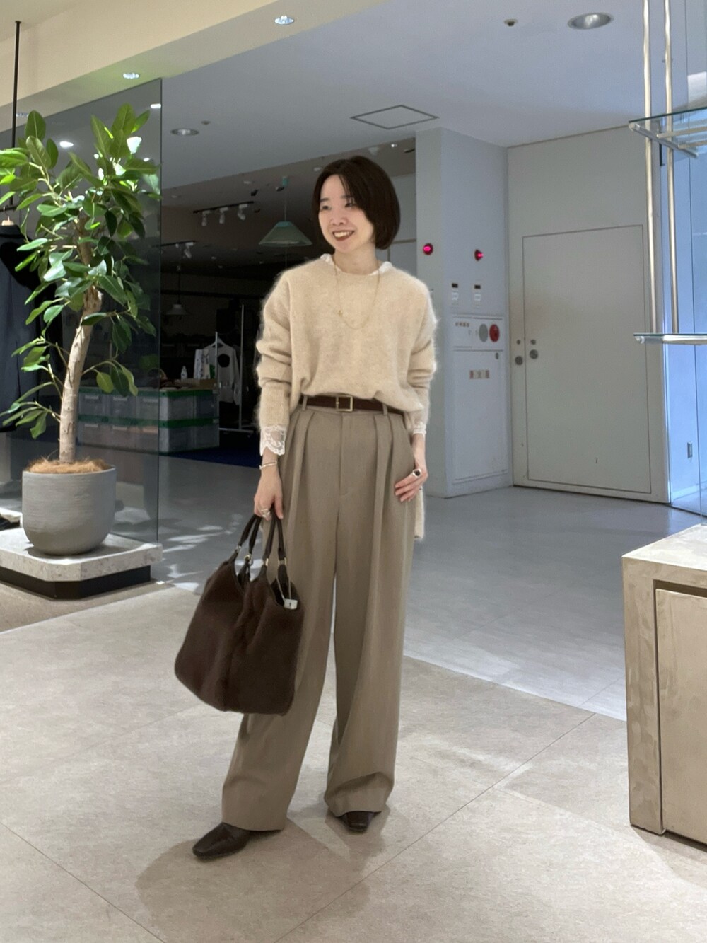 ブラウン系のトートバッグ、ベージュ系のスラックス、ブラウン系のブーツを着用したレディースの秋コーディネートの7枚目の写真