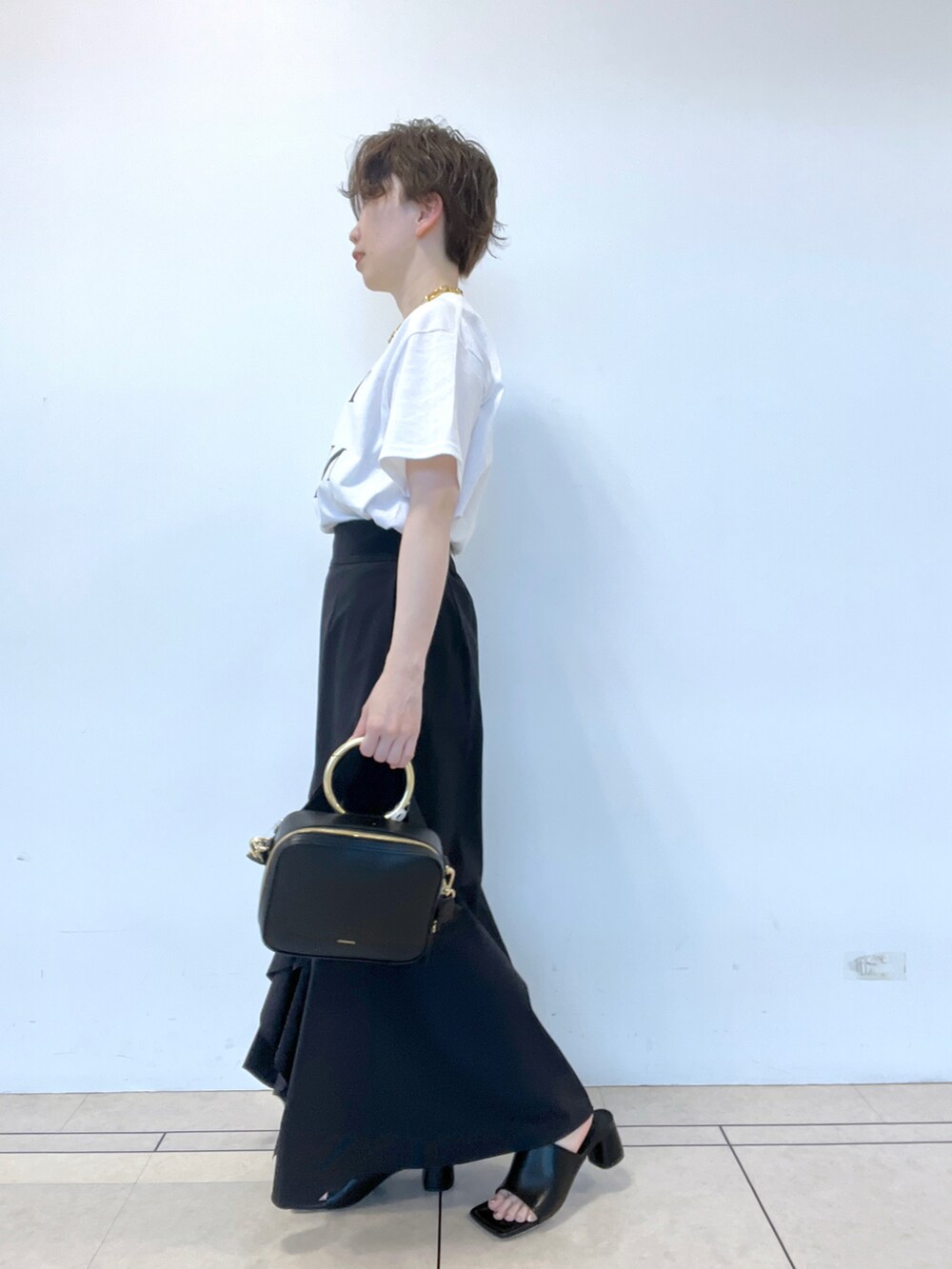 ブラック系のスカート、ホワイト系のTシャツ/カットソー、ブラック系のサンダルを着用したレディースの春コーディネートの2枚目の写真