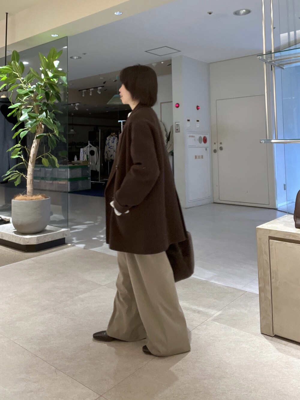 ブラウン系のトートバッグ、ベージュ系のスラックス、ブラウン系のブーツを着用したレディースの秋コーディネートの2枚目の写真