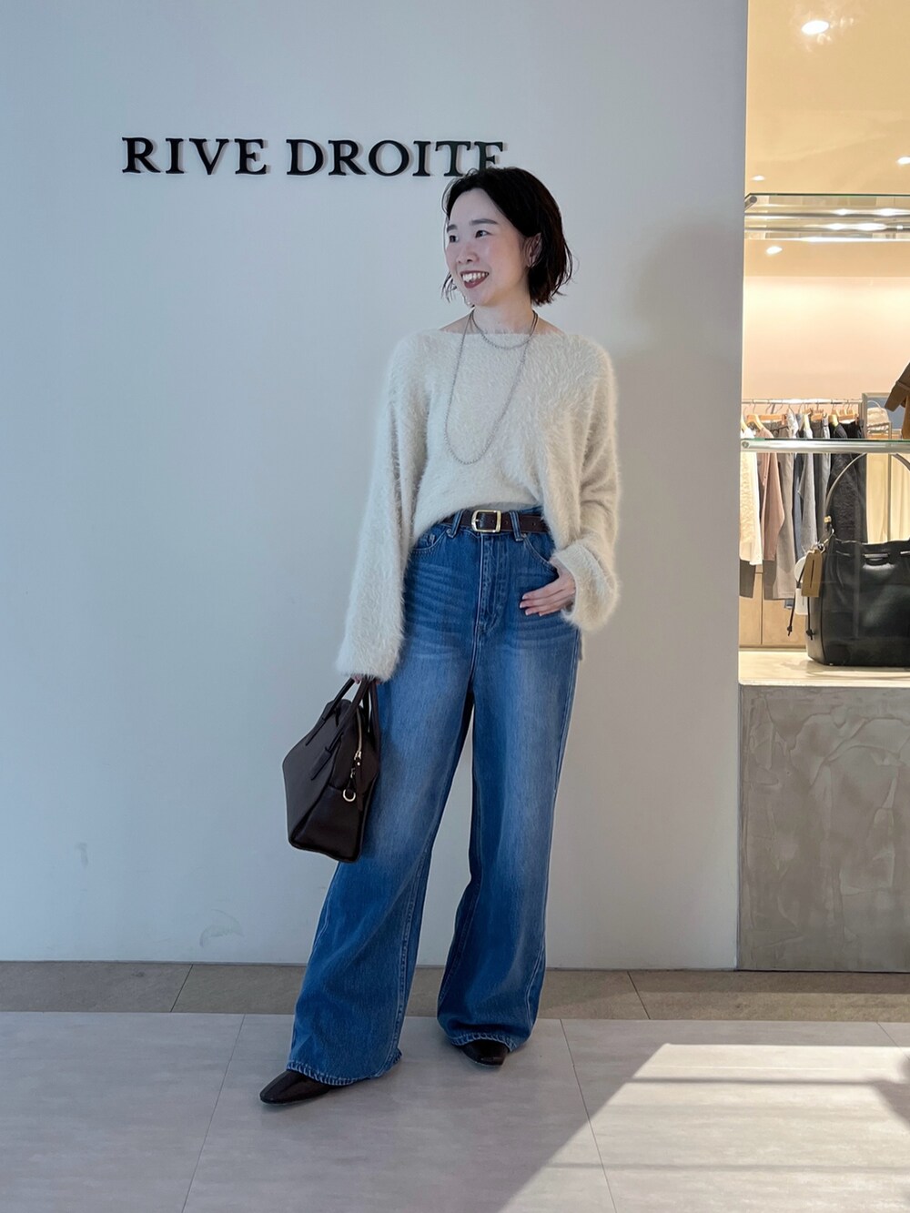 ブルー系のデニムパンツ、ホワイト系のニット/セーター、ブラウン系のボストンバッグを着用したレディースの秋コーディネートの2枚目の写真