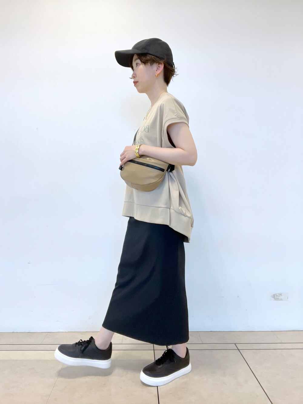 ブラック系のスカート、ベージュ系のTシャツ/カットソー、ベージュ系のボディバッグ/ウエストポーチを着用したレディースの春コーディネートの2枚目の写真