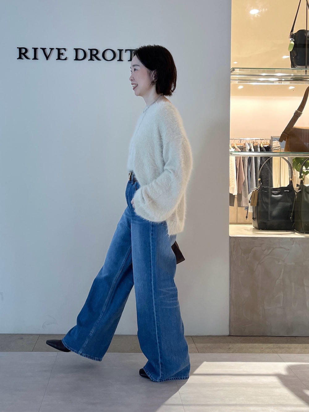 ブルー系のデニムパンツ、ホワイト系のニット/セーター、ブラウン系のボストンバッグを着用したレディースの秋コーディネートの3枚目の写真