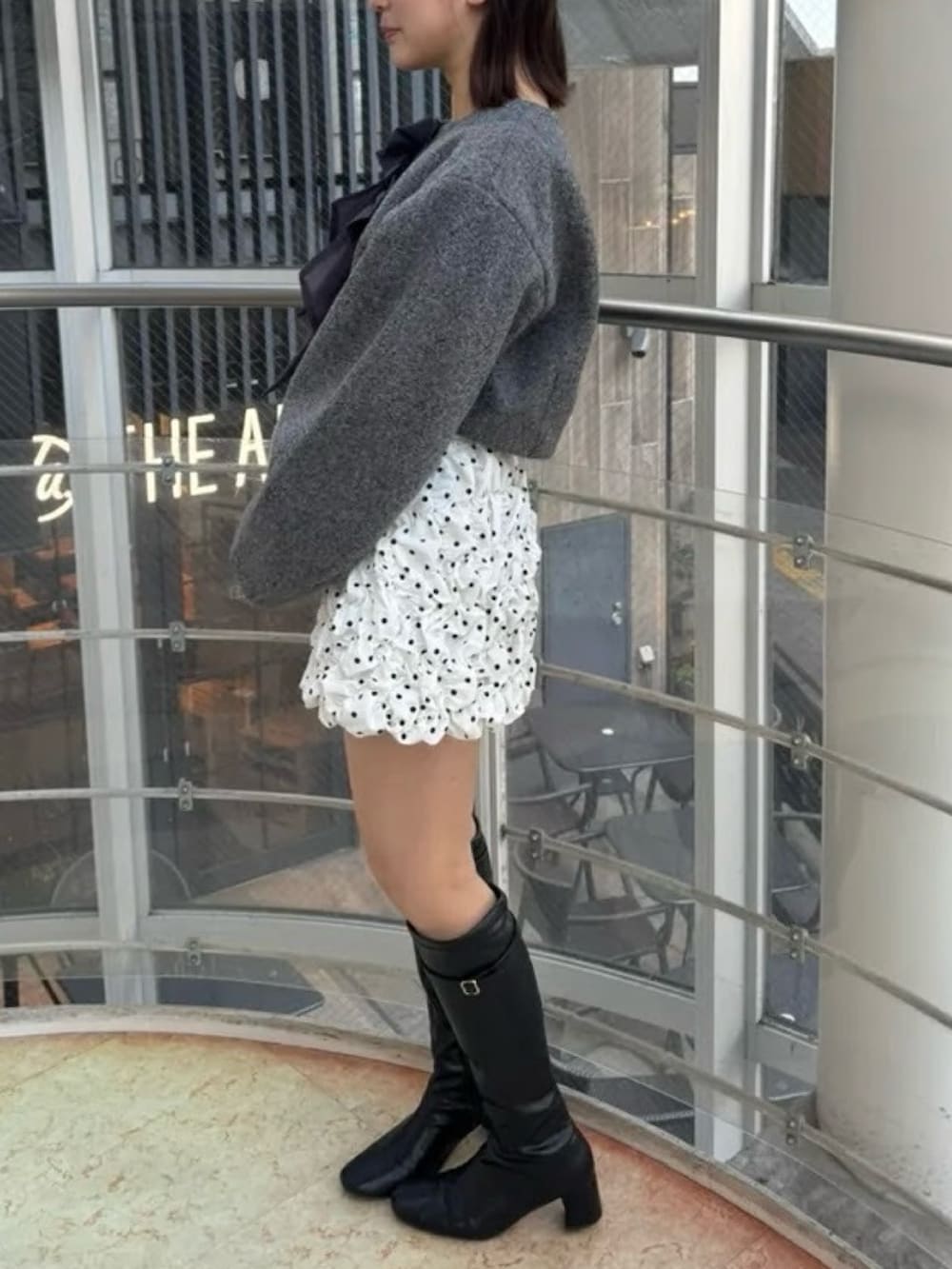 ホワイト系のスカート、グレー系のブルゾン、ブラック系のブーツを着用したレディースの冬コーディネートの2枚目の写真