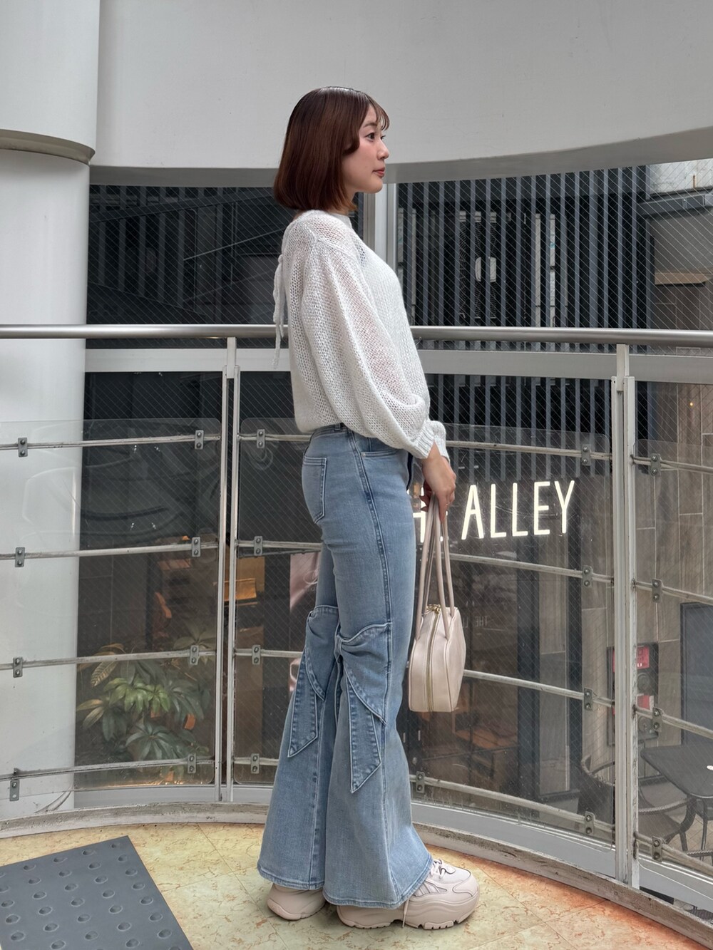 ブルー系のデニムパンツ、ホワイト系のニット/セーター、ホワイト系のハンドバッグを着用したレディースの春コーディネートの5枚目の写真