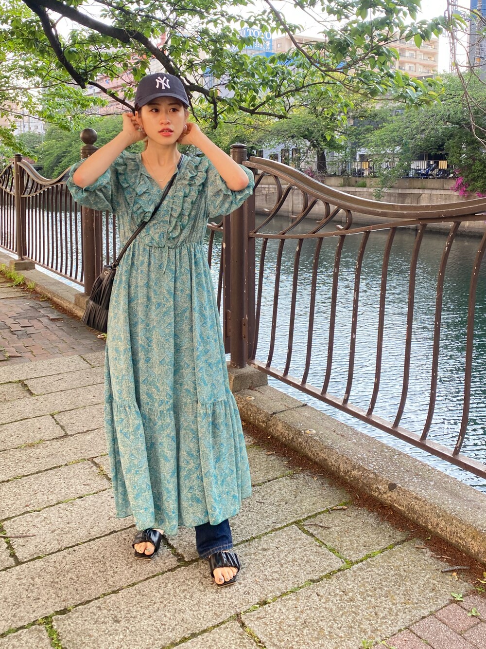 グリーン系のワンピース、ブラック系のサンダル、ブラック系のキャップを着用したレディースの春コーディネートの2枚目の写真