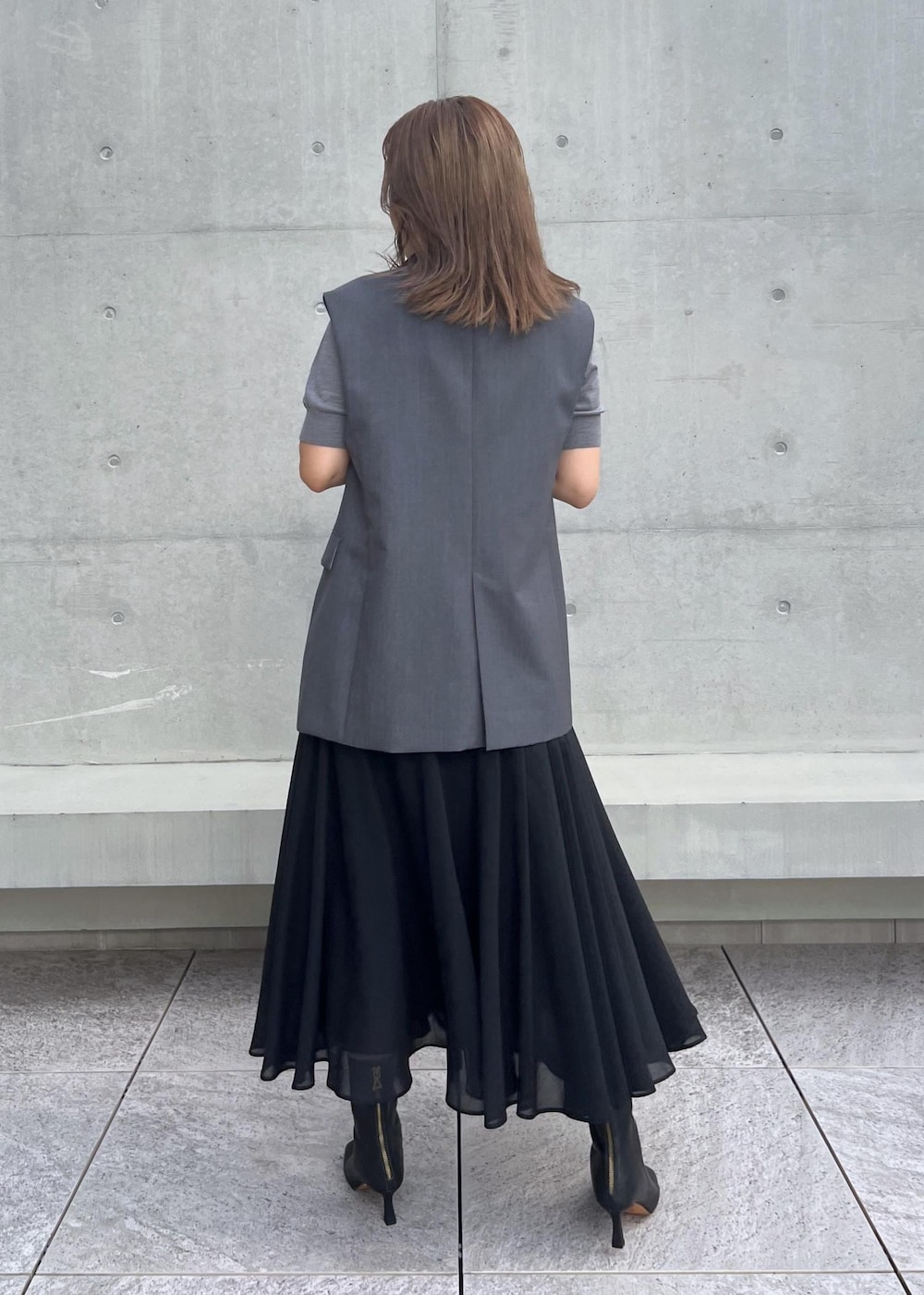 ブラック系のブーツ、ブラック系のスカート、グレー系のベストを着用したレディースの秋コーディネートの3枚目の写真