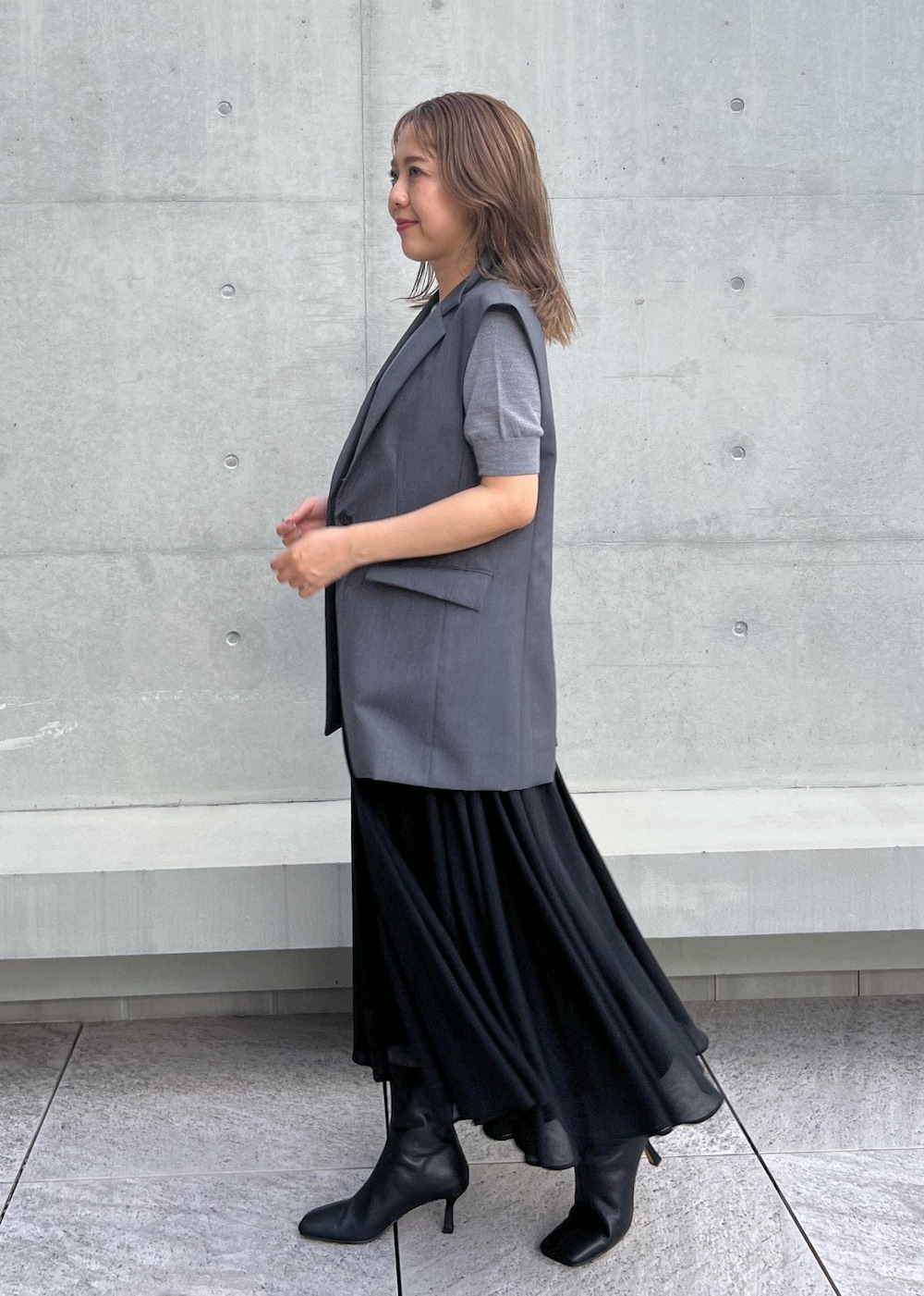 ブラック系のブーツ、ブラック系のスカート、グレー系のベストを着用したレディースの秋コーディネートの2枚目の写真