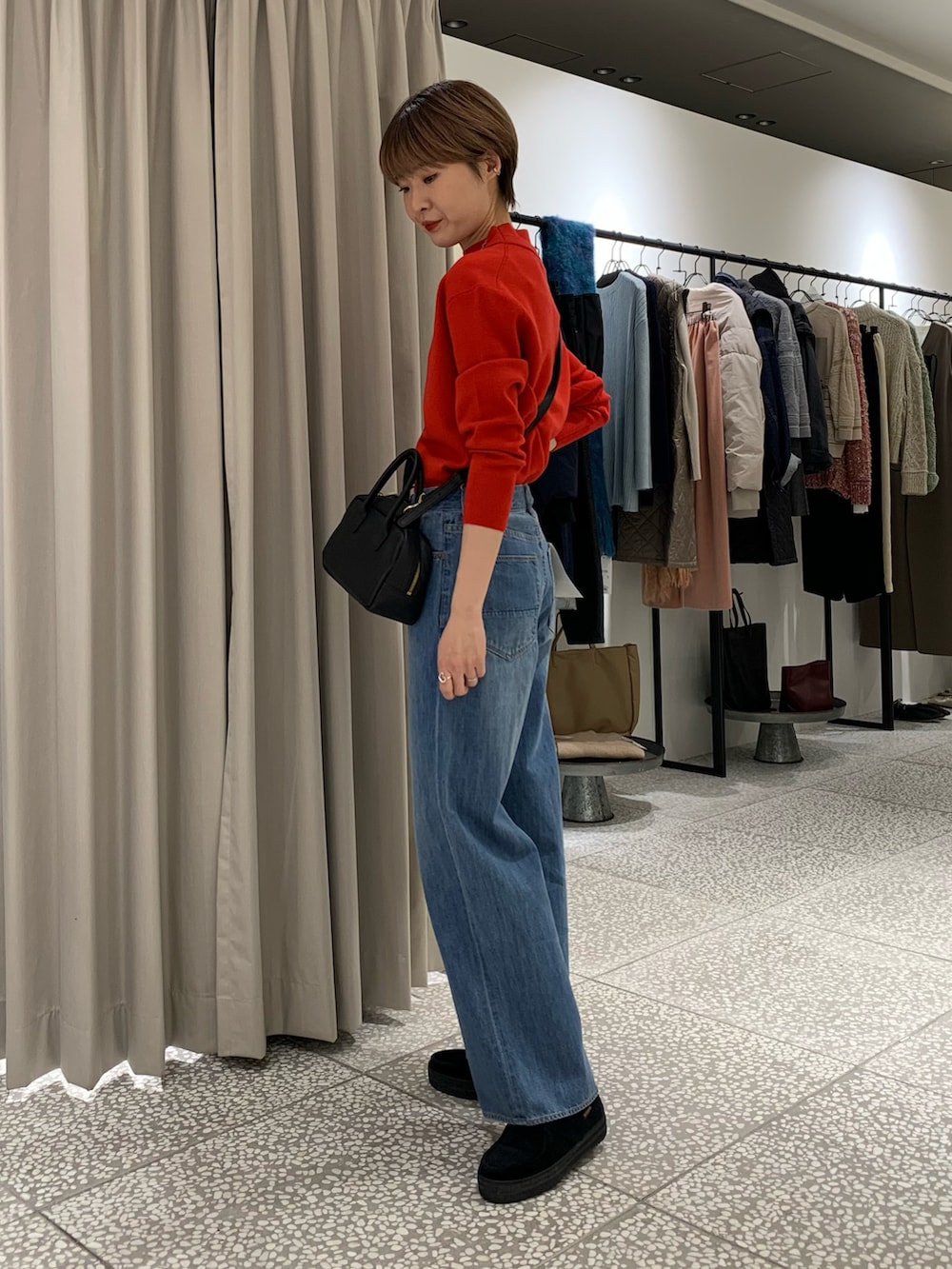 レッド系のニット/セーター、ブラック系のショルダーバッグ、ブルー系のデニムパンツを着用したレディースの冬コーディネートの2枚目の写真