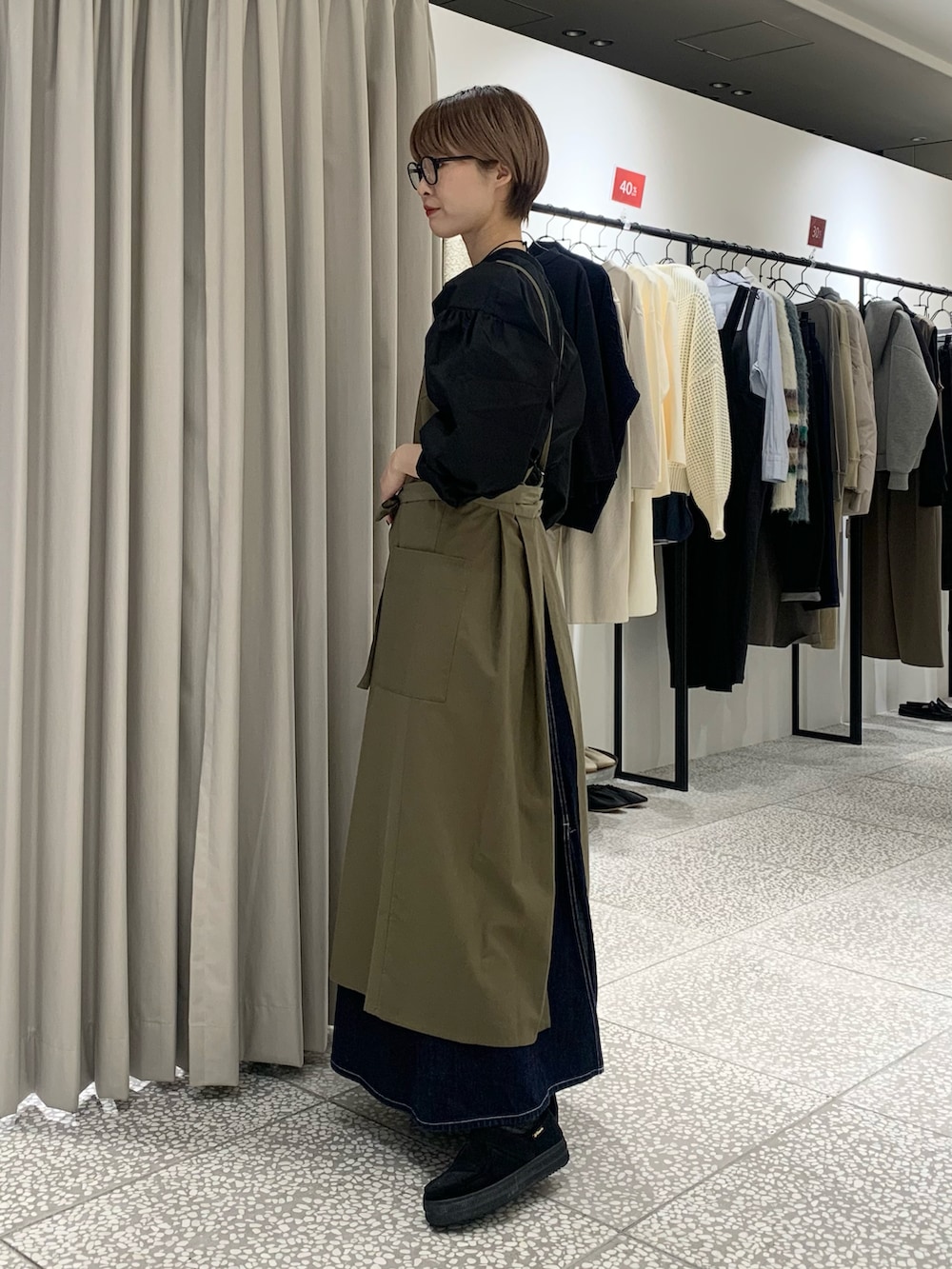 ブラック系のシャツ/ブラウス、ゴールド系のネックレス、グリーン系のエプロンを着用したレディースの冬コーディネートの2枚目の写真