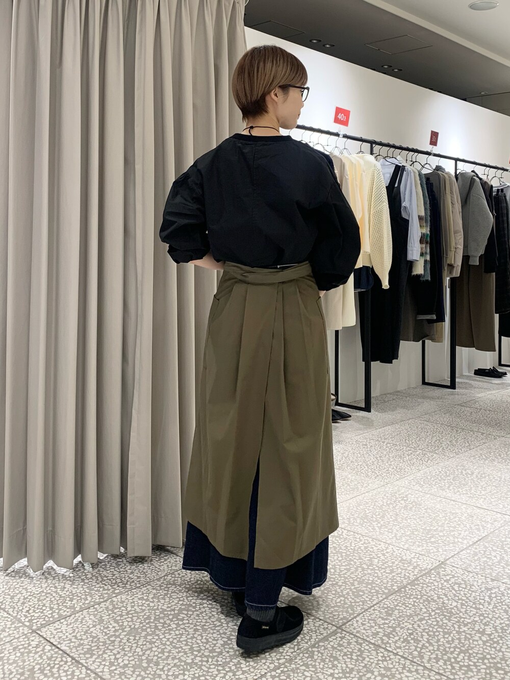 ブラック系のシャツ/ブラウス、ゴールド系のネックレス、グリーン系のエプロンを着用したレディースの冬コーディネートの5枚目の写真