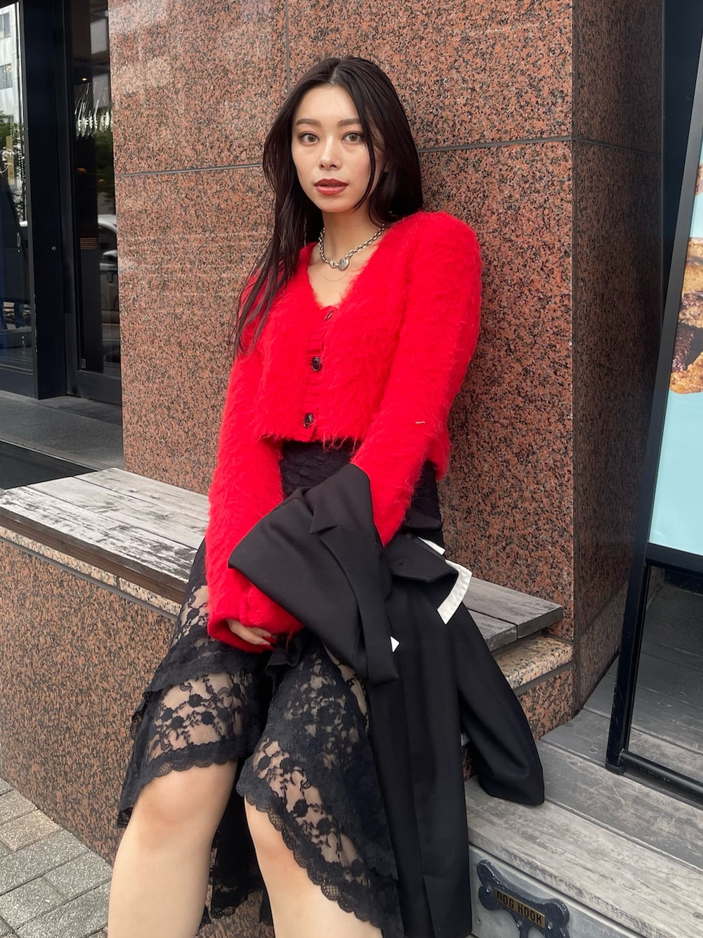 ブラック系のテーラードジャケット、レッド系のニット/セーター、ブラック系のスカートを着用したレディースの秋コーディネートの3枚目の写真