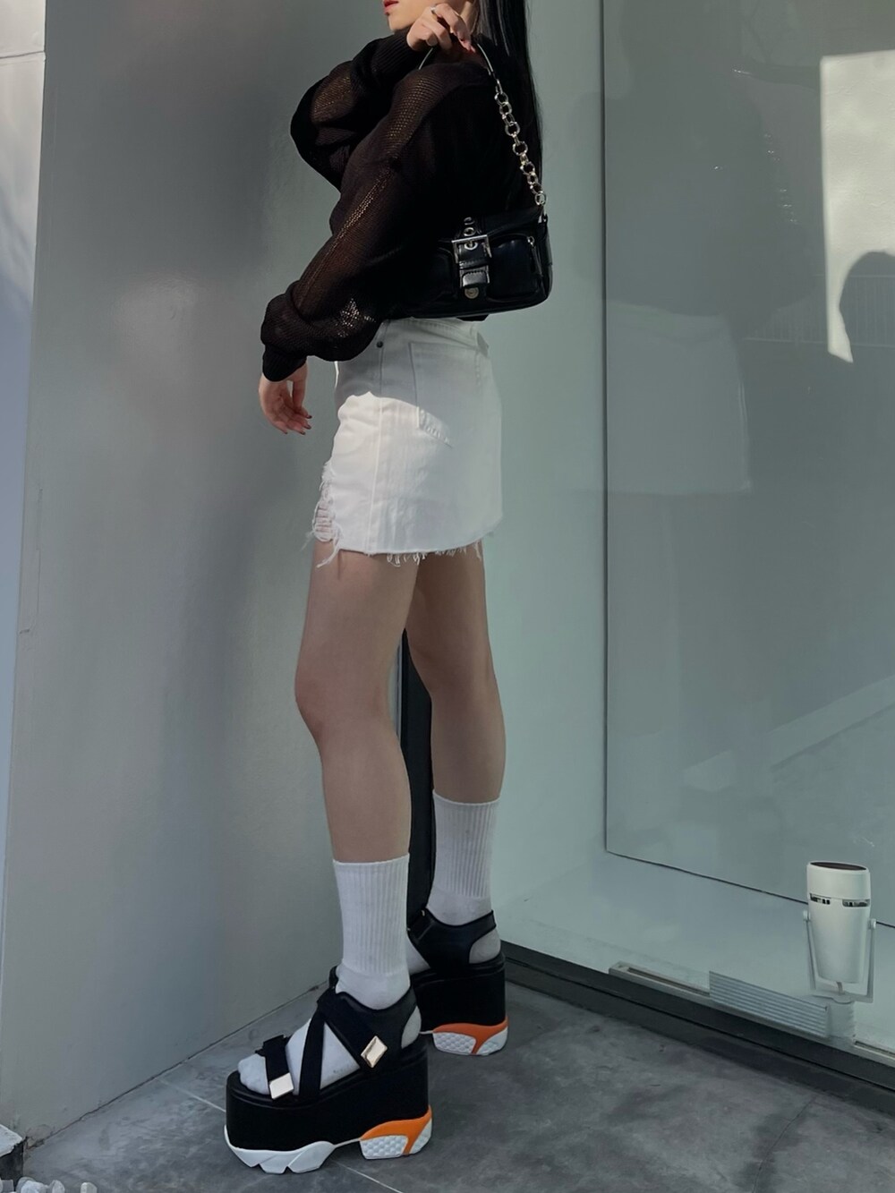 ホワイト系のデニムスカート、ブラック系のニット/セーター、ブラック系のサンダルを着用したレディースの春コーディネートの2枚目の写真