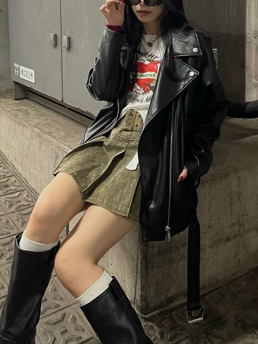 ブラック系のライダースジャケット、レッド系のTシャツ/カットソー、ベージュ系のスカートを着用したレディースの冬コーディネートの2枚目の写真