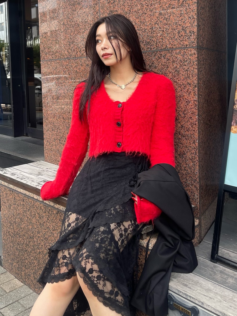 ブラック系のテーラードジャケット、レッド系のニット/セーター、ブラック系のスカートを着用したレディースの秋コーディネートの4枚目の写真