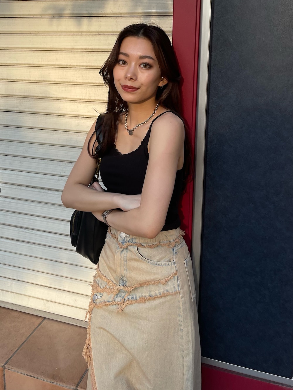 ブラック系のタンクトップ、ブルー系のデニムスカート、ブラック系のブーツを着用したレディースの夏コーディネートの2枚目の写真