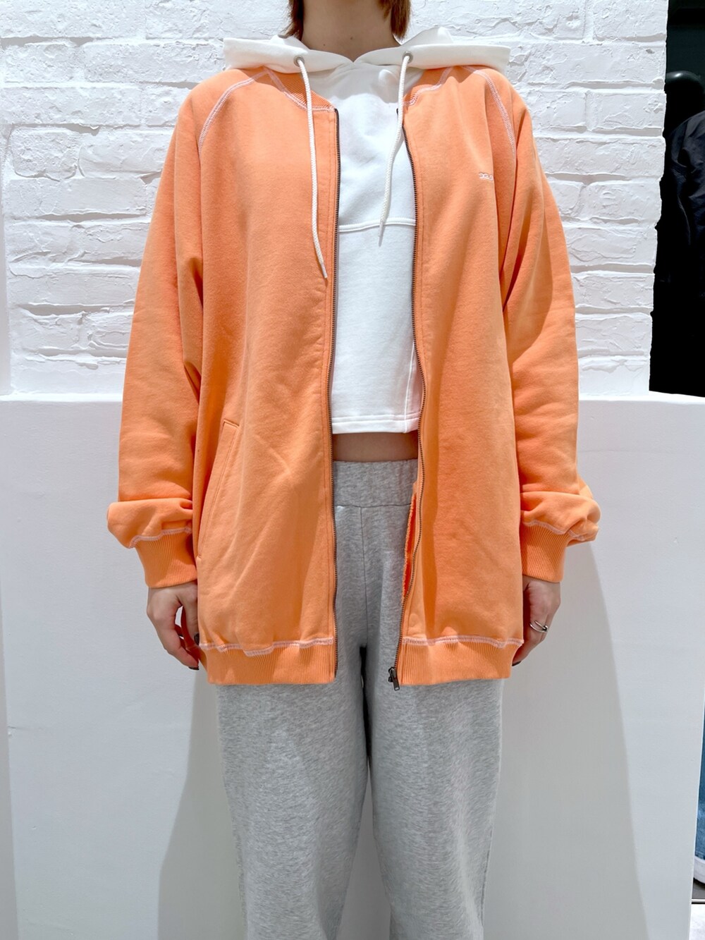 グレー系のスウェットパンツ、オレンジ系のスウェット、ホワイト系のパーカーを着用したレディースの春コーディネートの3枚目の写真