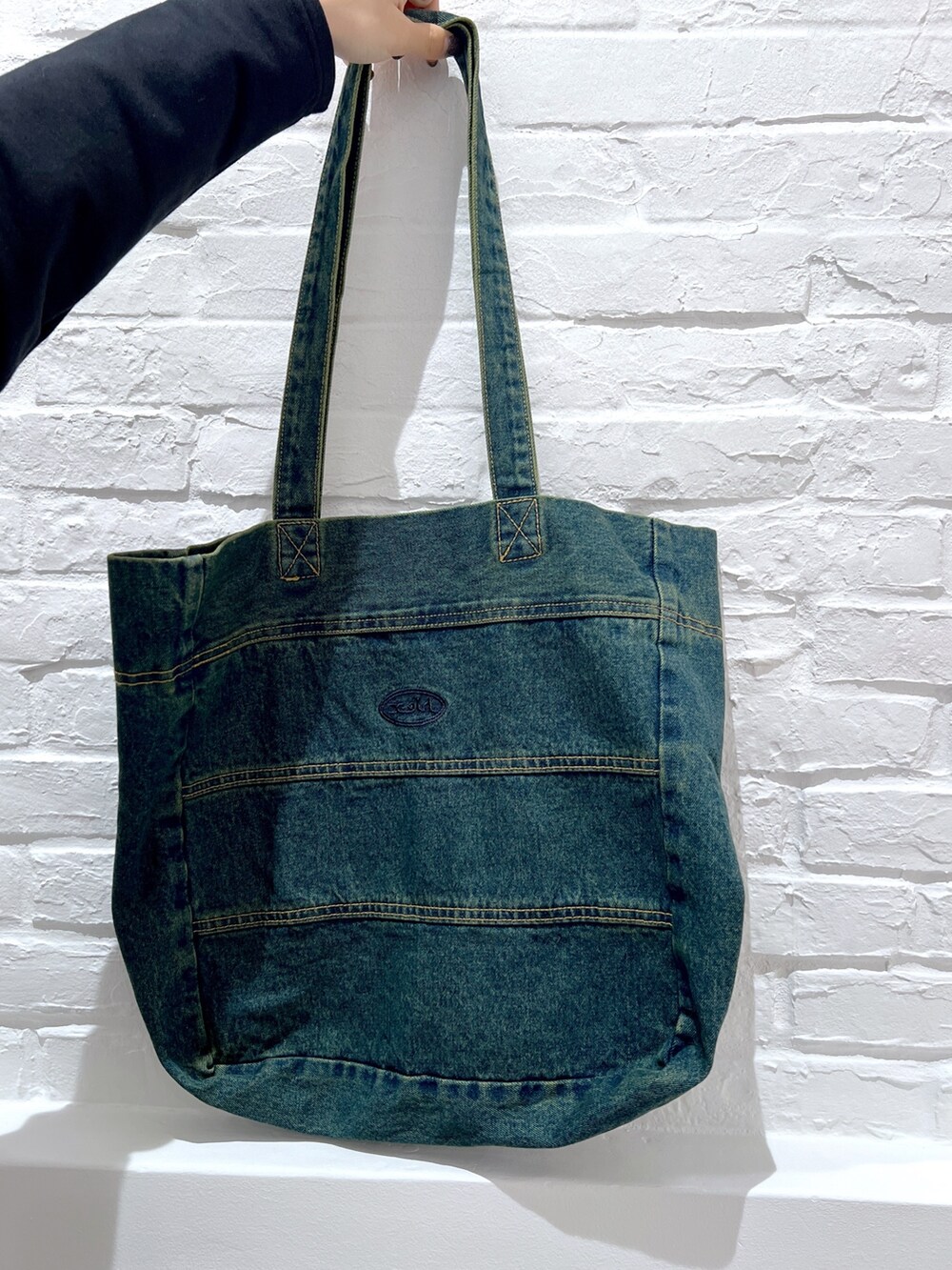 ブルー系のトートバッグ、ブラック系のワンピース、グリーン系のキャップを着用したレディースの春コーディネートの5枚目の写真