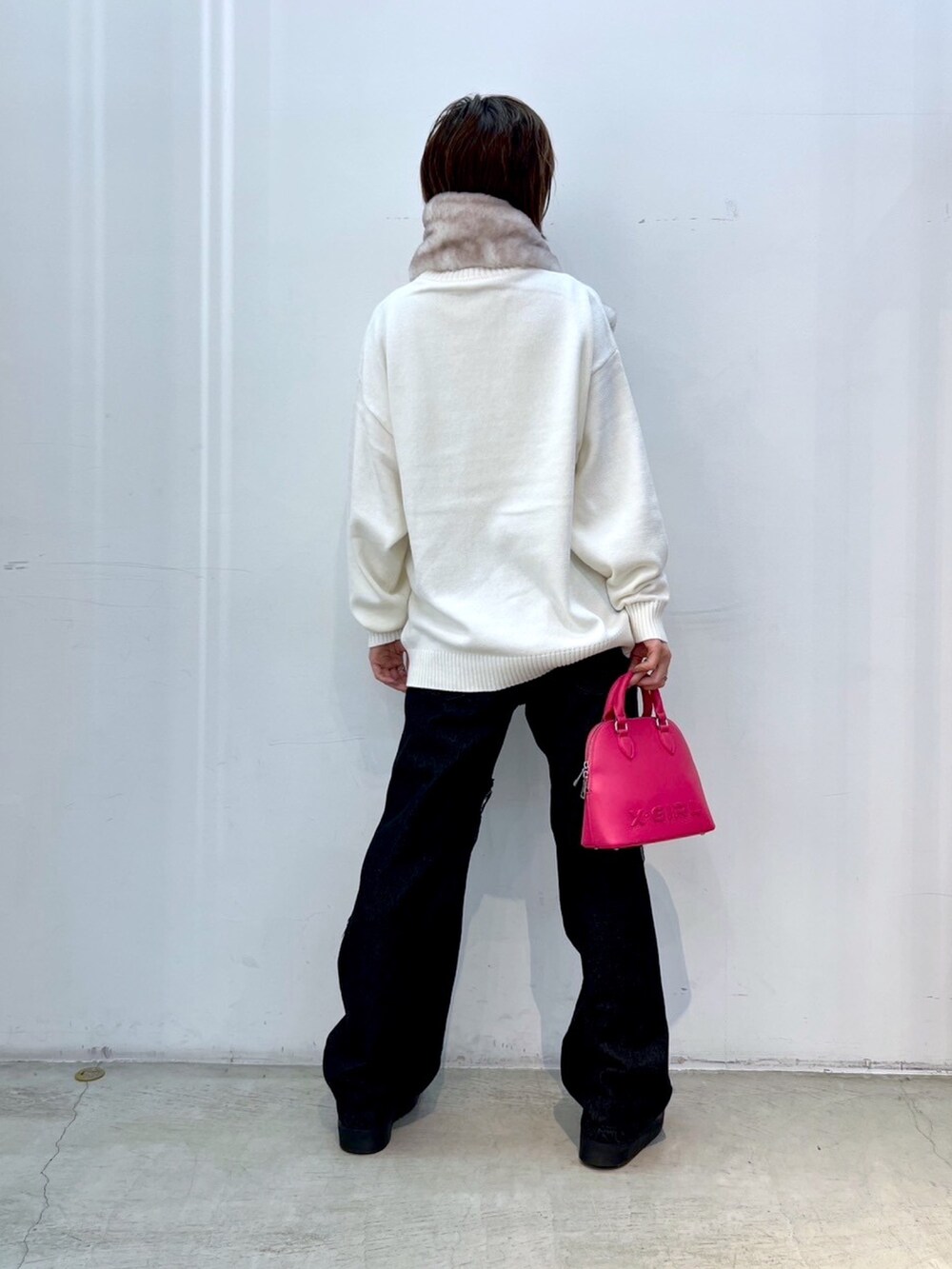 ブラック系のデニムパンツ、ピンク系のショルダーバッグ、ホワイト系のニット/セーターを着用したレディースの冬コーディネートの2枚目の写真