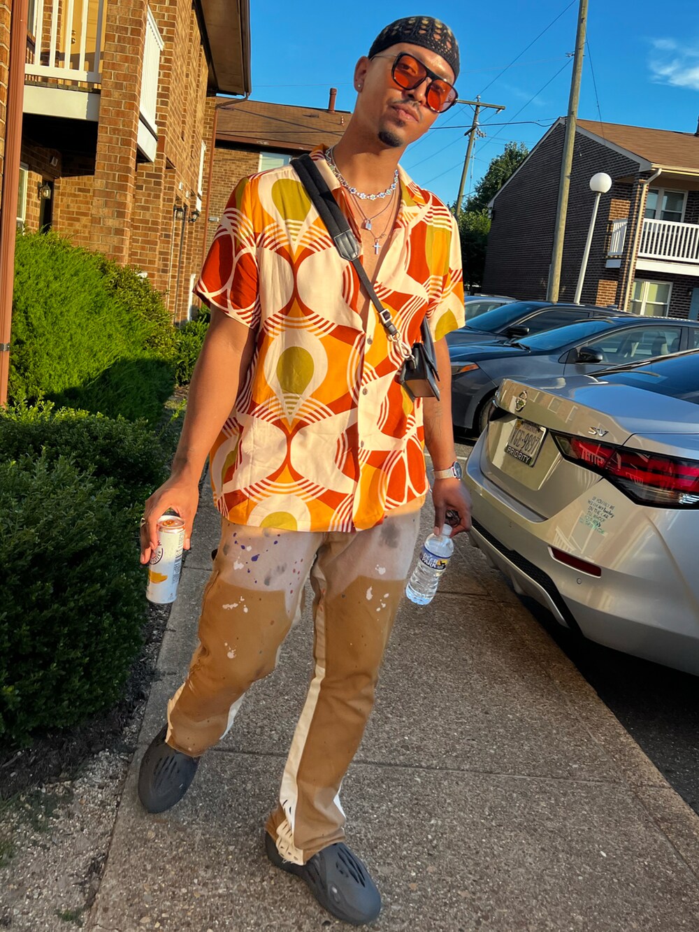 ブラウン系のスラックス、ブラック系のスニーカー、ブラック系のショルダーバッグを着用したメンズの夏コーディネートの2枚目の写真