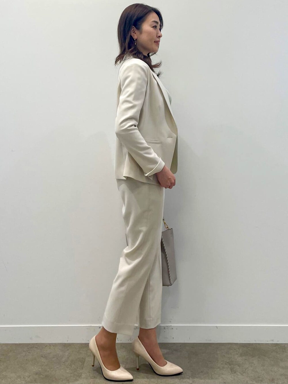 ベージュ系のスーツパンツ、グレー系のショルダーバッグ、グリーン系のニット/セーターを着用したレディースの春コーディネートの2枚目の写真