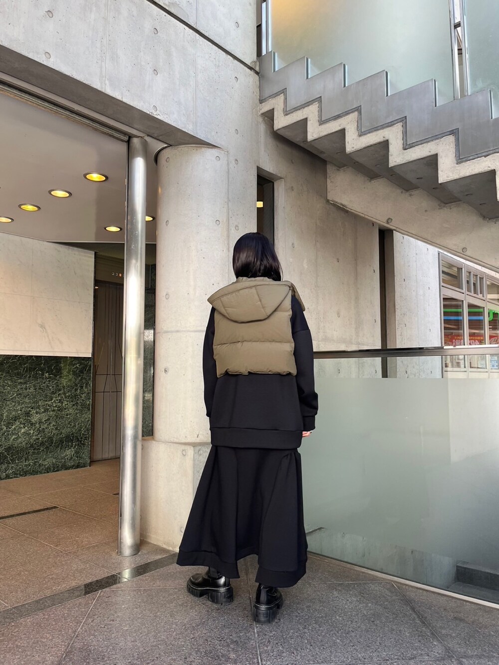 ブラック系のスカート、ブラック系のスウェット、グリーン系のダウンベストを着用したレディースの秋コーディネートの2枚目の写真