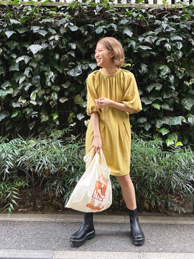 ブラック系のブーツ、イエロー系のエコバッグ/サブバッグ、グリーン系のワンピースを着用したレディースの春コーディネートの2枚目の写真