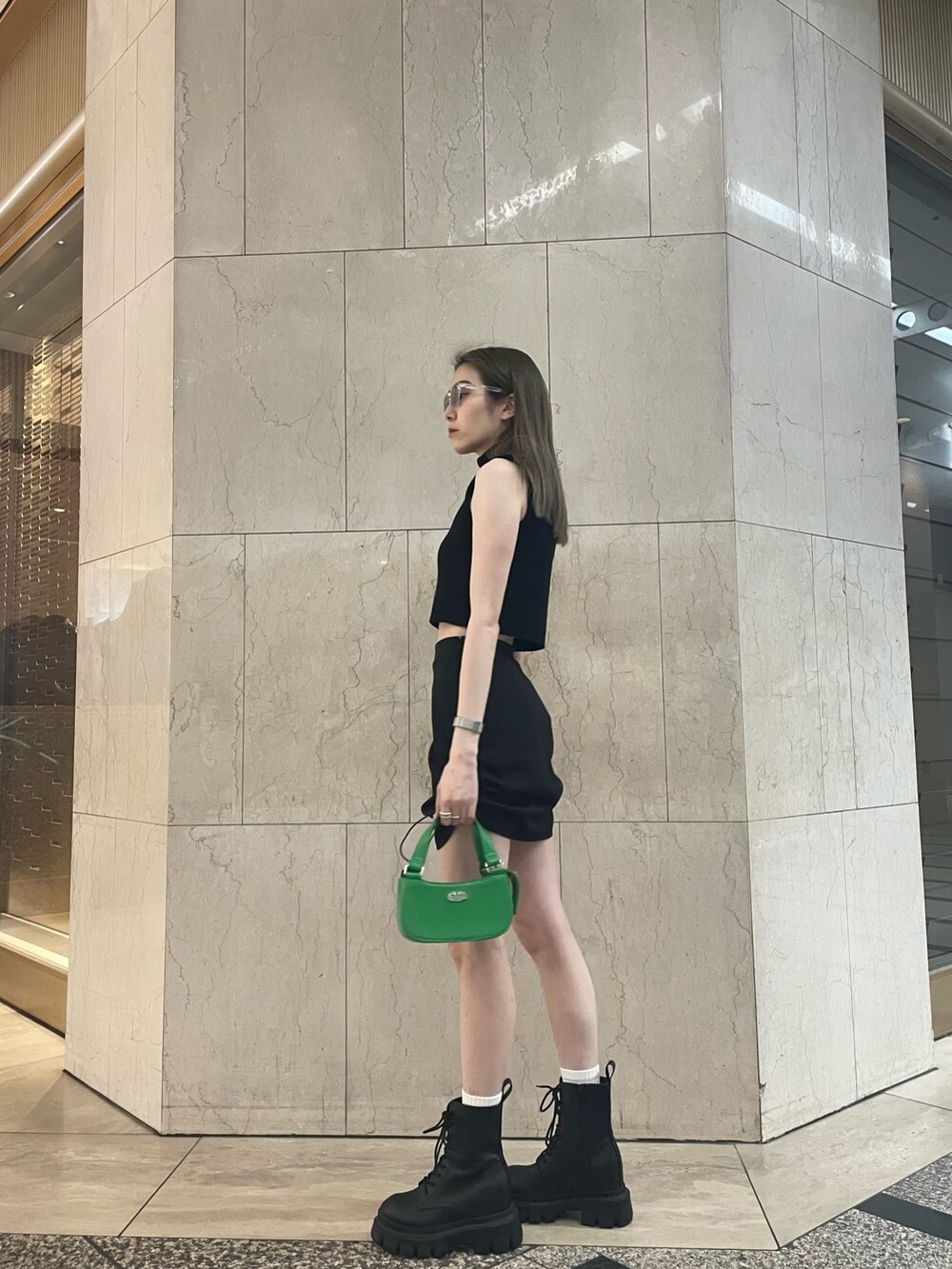 グリーン系のタンクトップ、ブラック系のスカート、ブラック系のブーツを着用したレディースの春コーディネートの3枚目の写真