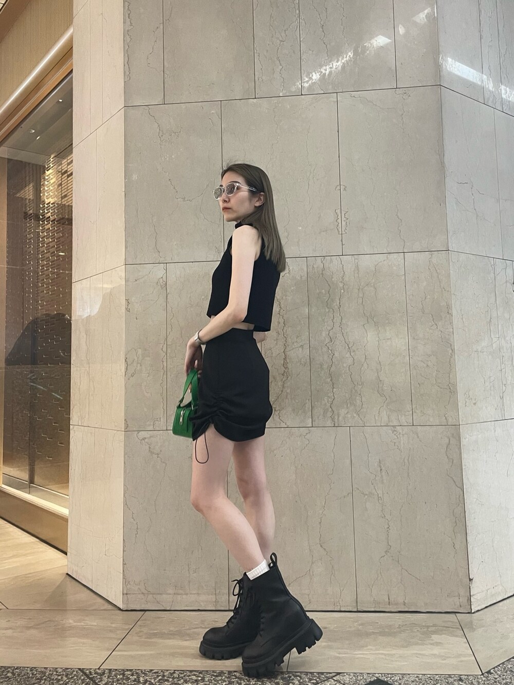 グリーン系のタンクトップ、ブラック系のスカート、ブラック系のブーツを着用したレディースの春コーディネートの2枚目の写真