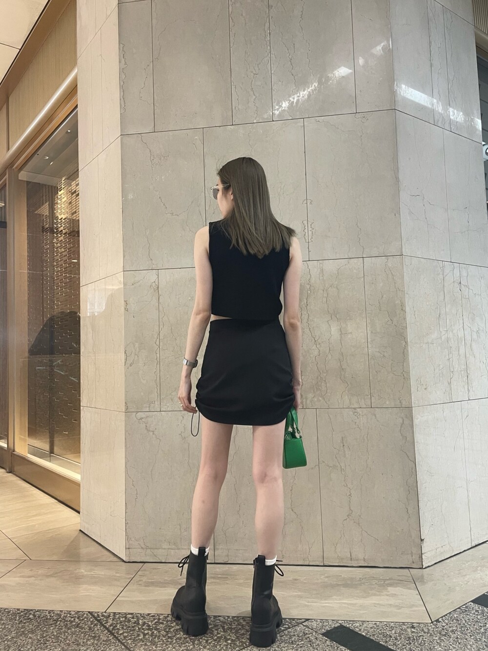 グリーン系のタンクトップ、ブラック系のスカート、ブラック系のブーツを着用したレディースの春コーディネートの4枚目の写真