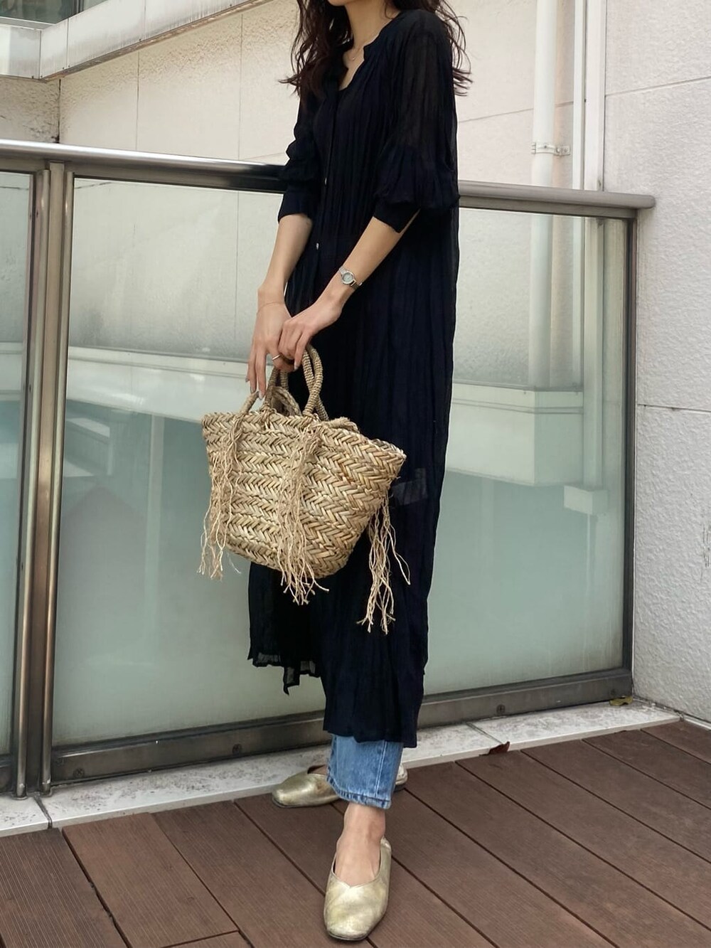 ブルー系のデニムパンツ、ブラック系のワンピース、ベージュ系のかごバッグを着用したレディースの春コーディネートの2枚目の写真