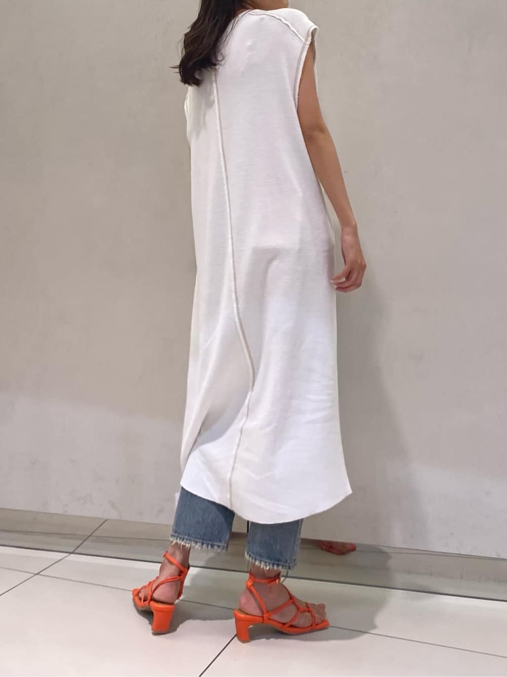 ブルー系のデニムパンツ、オレンジ系のサンダル、ホワイト系のワンピースを着用したレディースの夏コーディネートの2枚目の写真